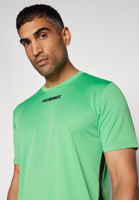 Roheline spordipusa, mis on valmistatud kergest kangast, ümmarguse kaelusega, lühikeste käistega ja mustade aktsentidega külgedel. Logo rinna piirkonnas.