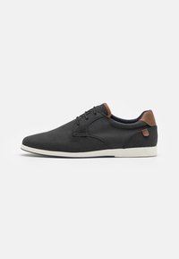 Chaussures noires perforées avec une texture lisse, dotées d'accents en cuir marron et de semelles en caoutchouc blanches. Design à lacets avec un bout arrondi.