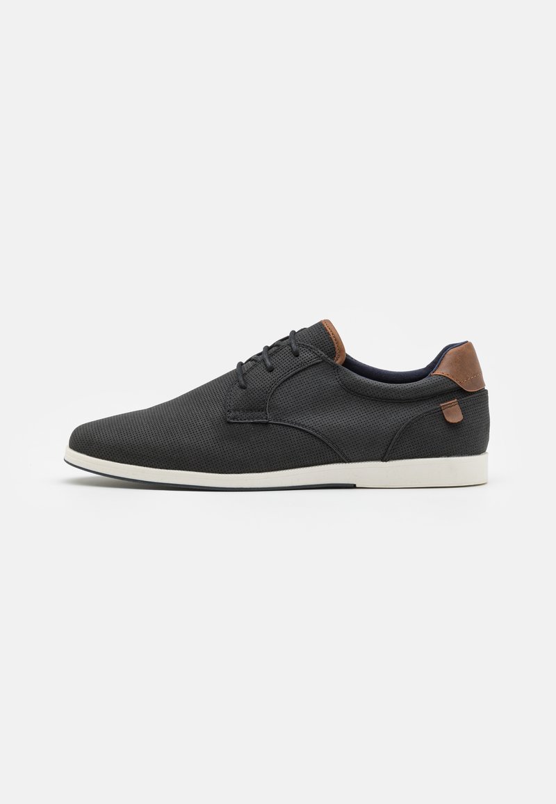 Chaussures noires perforées avec une texture lisse, dotées d'accents en cuir marron et de semelles en caoutchouc blanches. Design à lacets avec un bout arrondi.