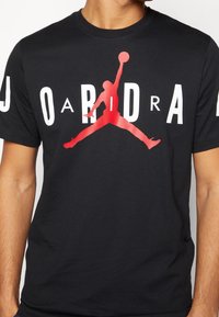 Czarna bawełniana koszulka z dużym czerwonym i czarnym logo JORDAN oraz sylwetką zawodnika dunkującego na przodzie, na środku.