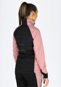 Taillierte Jacke aus einer Mischung von schwarzem und pinkem Stoff; verfügt über einen hohen Kragen und einen gepolsterten Rückenbereich; beinhaltet ein Logo in der Taille.