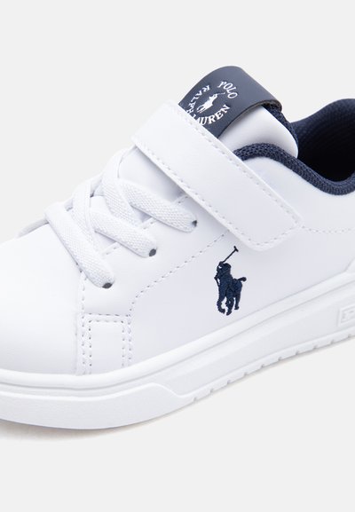 Zapatilla blanca de piel con interior azul marino, logo de Polo Ralph Lauren en el lateral, cordones blancos y cierre de velcro blanco.