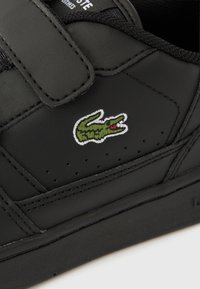 Μαύρο αθλητικό παπούτσι με συνθετικό υλικό, ιμάντα με βέλκρο, υφασμάτινα πάνελ και ραμμένες λεπτομέρειες. Διαθέτει κεντημένο πράσινο λογότυπο κροκόδειλου στο πλάι.