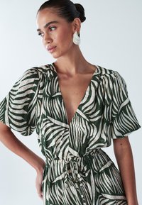 Roheline ja kreemikas troopilise mustriga kleit lühikeste paffvarrukatega, sügava V-kaelusega ja elastse vöökohaga, millel on seotud detail.