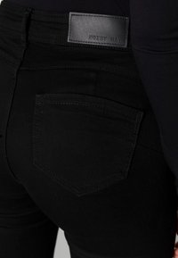 Svarta smala jeans med en slät textur, med en bakficka och en svart läderetikett som säger "NOISY MAY" på midjebandet.