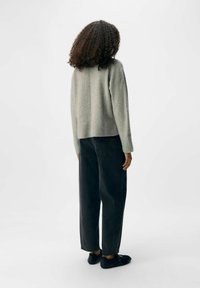 Grå, texturerad tröja med boxig passform, kombinerad med svarta, löst sittande jeans och svarta flats, sedd bakifrån mot en enfärgad bakgrund.