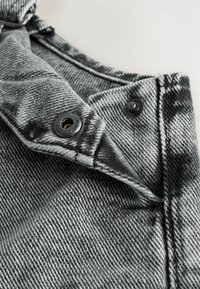 Chaqueta de mezclilla en negro y gris con un acabado texturizado. Cuenta con botones de metal y detalles de costura que destacan el patrón de la tela.