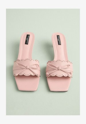 Rúžové sandále na plochom podpätku so štvorcovou špičkou, ktoré majú vlnitý remienok s perforáciami a detailom mašličky na hornej časti. Hladká kožená textura.