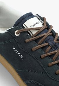 Zapatillas de ante en color marino con cordones marrones, parte superior texturizada, etiqueta de logo blanca y suela de goma beige. Presenta detalles cosidos y ojales.