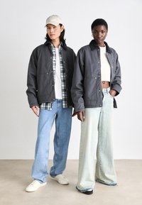 Grå jakker med trykknapper, båret over en hvid skjorte og plaidlag. Lys blå og denim jeans med markante pasformer og teksturer.