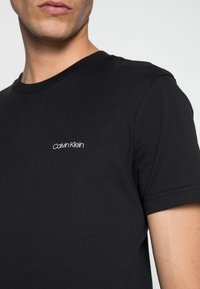 Svart bomull t-shirt med klassisk rund halsringning, korta ärmar och en liten vit "Calvin Klein"-logotyp på bröstet.