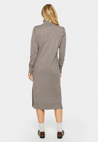 Abito grigio a collo alto in maglia con maniche lunghe, spacchi laterali e orlo a coste. La texture è morbida, con una silhouette dritta che arriva sotto il ginocchio.