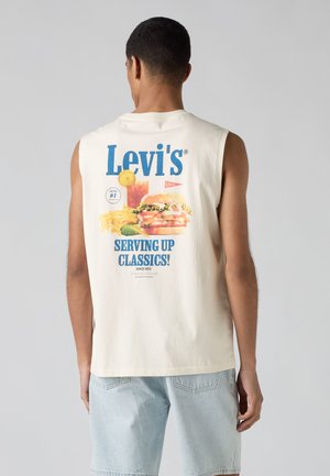 Homme portant un débardeur blanc Levi's avec un graphisme de burger, frites et boisson et le texte « Serving up classics ! » dans le dos.