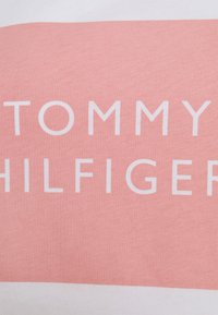 Tela de algodón rosa y blanca con un gran y audaz logotipo "TOMMY HILFIGER" en blanco. Textura suave con un ligero brillo. Rayas horizontales.