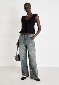 Black sleeveless top with ruffled neckline; light blue wide-leg jeans with metallic studs; black shoes; small gray handbag.
