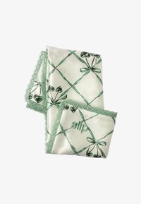 Mascherina da notte in seta con base crema decorata da nastri verdi e motivi a cuore, rifinita con un delicato pizzo verde e con il nome del marchio ricamato.