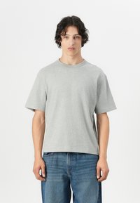 Grå t-shirt med korte ærmer lavet af blødt stof, har en klassisk rund hals, afslappet pasform og minimalistisk design. Båret med blå jeans.