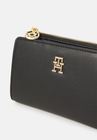 Black leather wallet with a gold zipper and hardware. Features a prominent gold logo and smooth texture. Compact and rectangular shape.