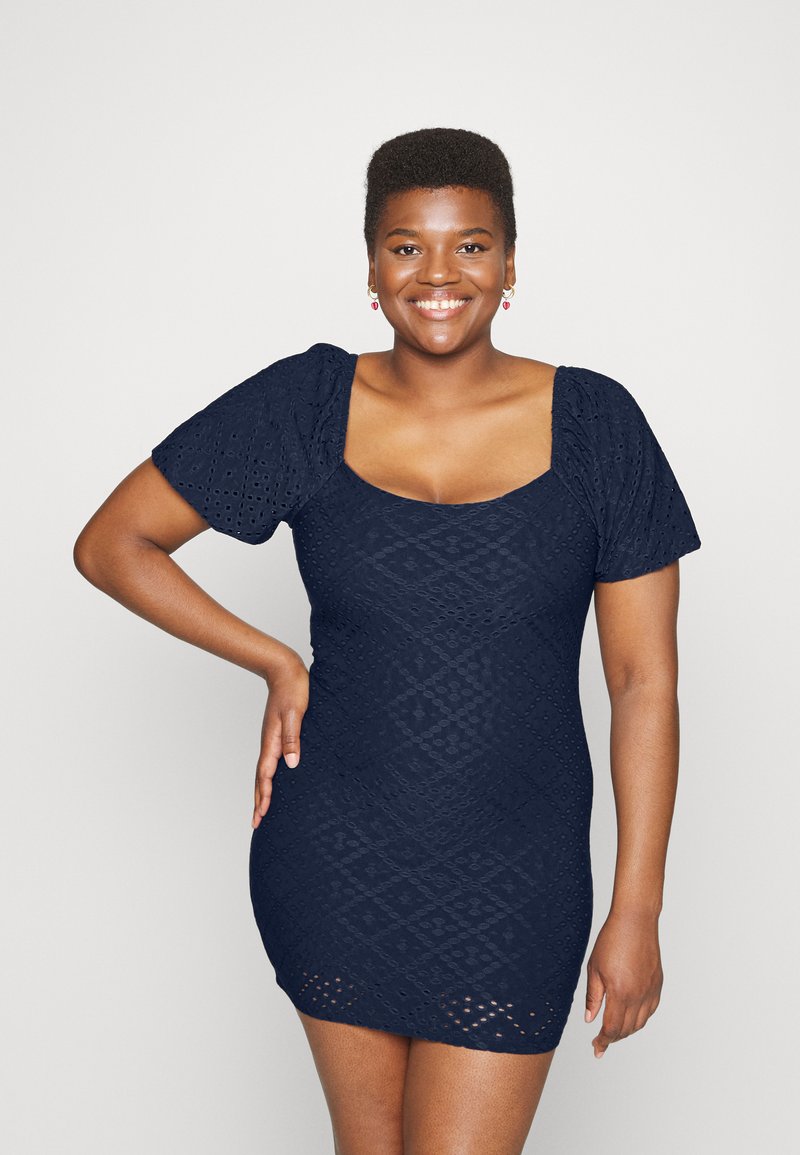 Vestido de malha azul-marinho com um padrão de diamante texturizado, apresentando mangas bufantes e um decote quadrado. Silhueta curta e ajustada.