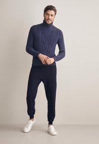 Mörkblå stickad polotröja med flätmönster, kombinerad med mörka joggers och vita sneakers. Slät tygkvalitet och avslappnad passform.