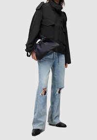 Zwarte cropped jas met grote voorzakken, gecombineerd met lichtblauwe distressed wijde broek met gescheurde knieën en puntige zwarte schoenen.