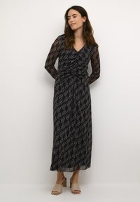 Črna dolga obleka s dolgimi rokavi, okrašena s geomtričnim vzorcem v bež barvi. Narejena iz prozornega materiala z ovitim dizajnom in zoženim pasom.