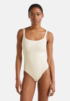 Lichtbeige badpak met vierkante halslijn, dikke banden en een gladde, rekbare textuur. Hoog uitgesneden beenopening voor een slanke uitstraling.