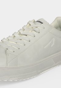 Baskets basses blanches avec lacets blancs, semelle texturée et logo discret de la marque sur le côté et la languette.