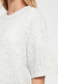 Ανοιχτό γκρι πλεκτό πουλόβερ με υφασμένο σχέδιο, κοντά μανίκια και στρογγυλή λαιμόκοψη. Μαλακό ύφασμα με διακριτικό ριμπ ύφανση κοντά στο τελείωμα.