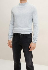 Suéter de punto gris claro con cuello redondo, puños de canalé y dobladillo. Combinado con jeans de mezclilla oscuros de corte estándar.