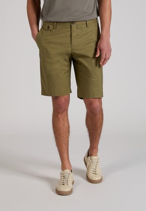 Man draagt olijfgroene korte broek tot op de knie met zakken met knopen, een grijs T-shirt en beige sneakers met bruine zolen.