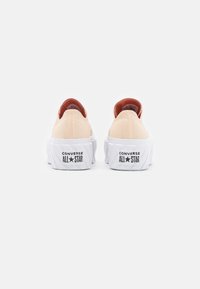 Paire de baskets basses beige Converse All Star vues de dos avec des semelles plateformes épaisses blanches et un texte de logo noir.