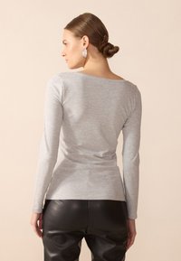 Top de manga larga gris hecho de una tela suave, con un escote de barco y una silueta ajustada. Combinado con pantalones de cuero negros.