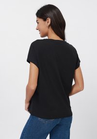 T-shirt en coton noir à manches courtes déroulées, offrant une coupe décontractée et un col rond. Texture lisse et design simple.