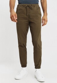 Kaki joggerbyxor med elastiska muddar och midja, utrustade med snörning. Tillverkade av mjuk tyg, med sidofickor för funktionalitet.