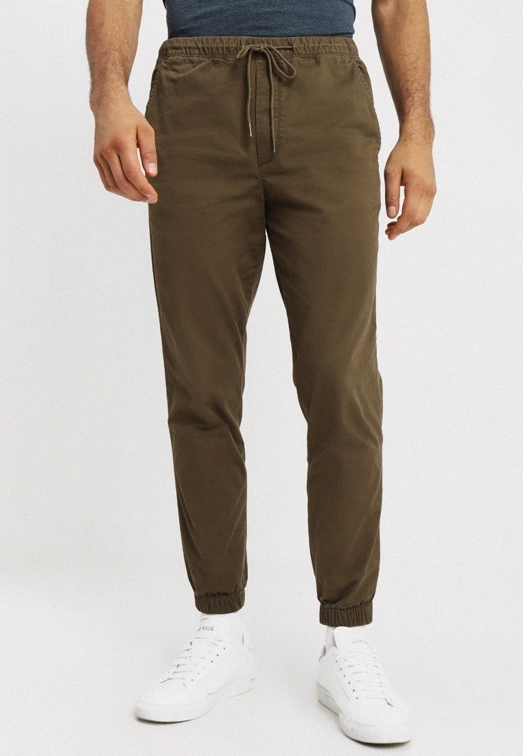 Kaki joggerbyxor med elastiska muddar och midja, utrustade med snörning. Tillverkade av mjuk tyg, med sidofickor för funktionalitet.