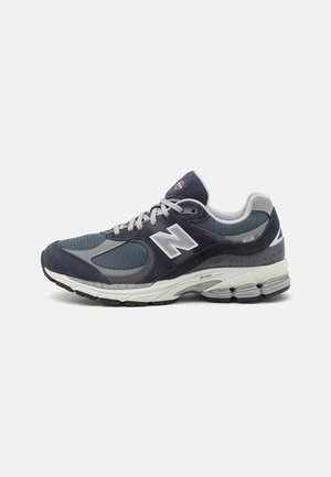 Sapatilhas New Balance com parte superior em malha e camurça azul-marinho, detalhes cinza, logótipo branco, sola almofadada e pormenores texturizados.
