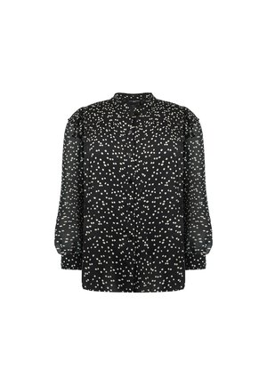 Blouse noire à manches longues transparentes, motif à pois blancs, col rond, et patte de boutonnage à l'avant. Présente des détails subtils de fronces aux épaules.