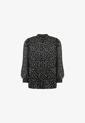 Blouse noire à manches longues transparentes, motif à pois blancs, col rond, et patte de boutonnage à l'avant. Présente des détails subtils de fronces aux épaules.
