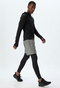 Svart atletisk långärmad tröja med huva, grå shorts, svarta leggings och svarta sneakers. Tyget verkar lätt och åtsittande.