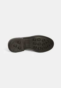 Schwarze Gummisohle mit kreisförmigem Grip-Muster, ausgestattet mit erhabenen Punkten für besseren Halt. Glatte Oberfläche und abgerundete Zehenform.