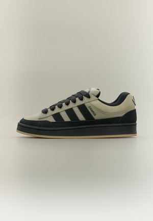 Baskets basses beige et noir avec lacets noirs, trois bandes noires, texte "CAMPUS" et semelle en gomme sur fond neutre.