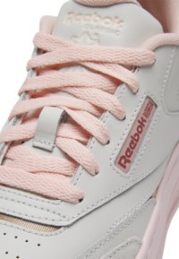 Baskets Reebok Classic avec une tige en cuir blanc, des lacets roses texturés et un petit patch logo avec des accents rouges et bleus.