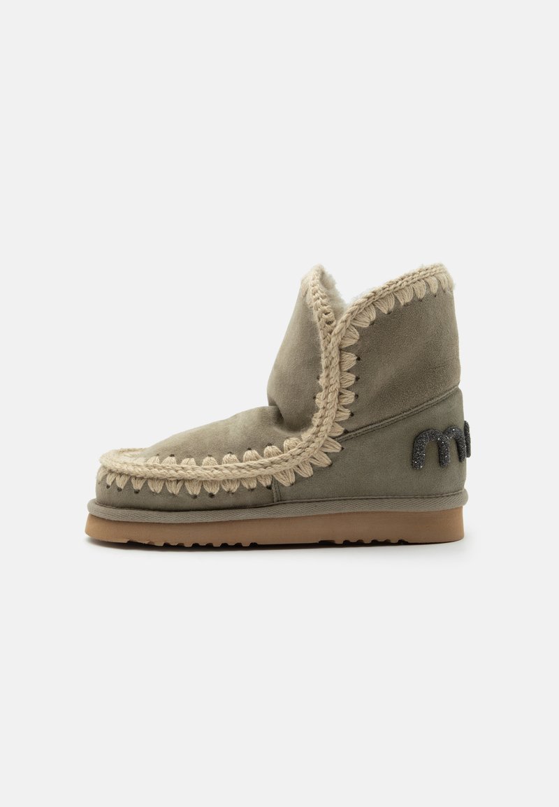 Bottine en daim gris avec bordure beige au crochet, doublure moelleuse, semelle plate en caoutchouc marron et logo noir brodé sur le talon.