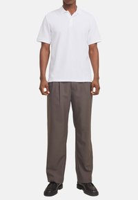 Polo shirt blanc à manches courtes avec un tissage texturé, associé à un pantalon ample taille haute marron foncé et des chaussures noires.