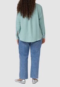 Hellblau strukturierte Langarmbluse, kombiniert mit lockeren blauen Jeans. Silberne Ballerinas mit glatter Oberfläche.