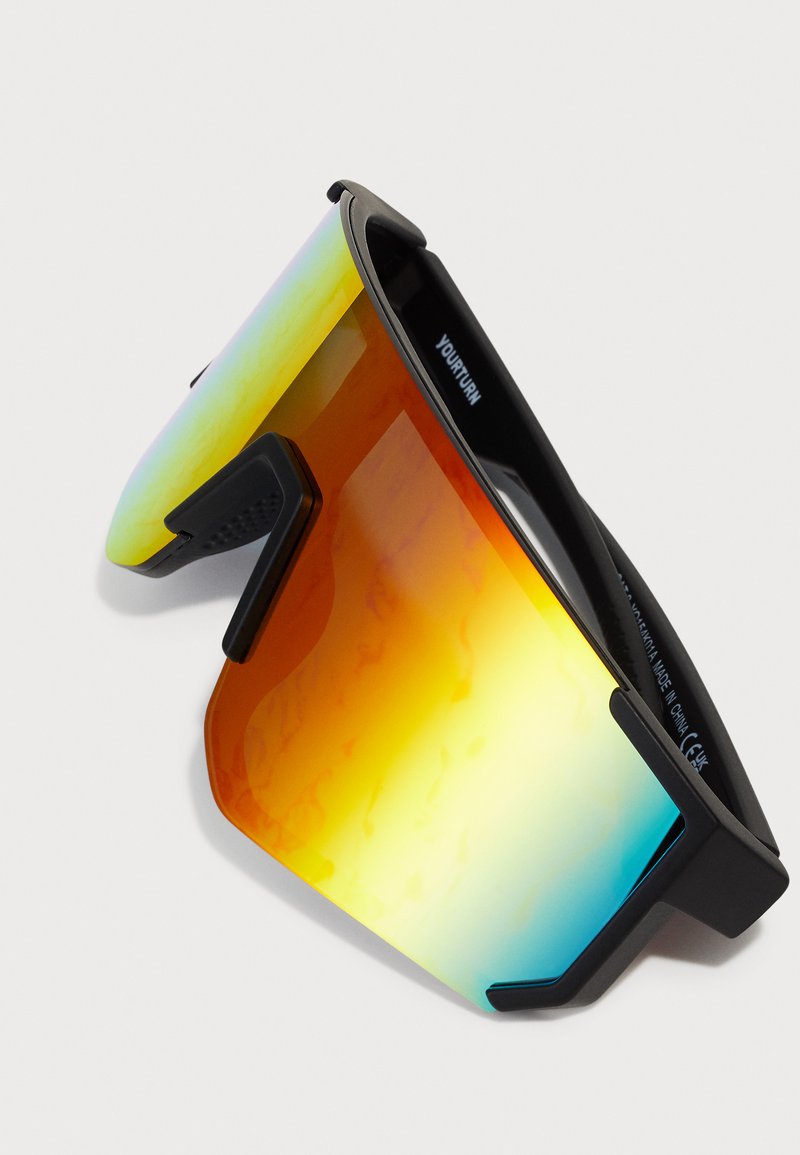 Gafas de sol deportivas con montura negra, lentes de gran tamaño en degradado de naranja a azul, que cuentan con acentos laterales texturizados y un diseño envolvente.