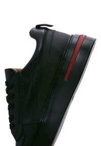 Baskets en cuir noir avec un dessus texturé, fermeture à lacets et accent rouge sur la semelle. Présente une semelle plate et épaisse ainsi qu'une languette au talon.