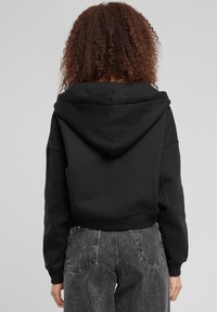 Hoodie corto nero con un grande cappuccio, polsini e orlo a costine. Abbinato a jeans grigi a vita alta con texture e tasche posteriori.