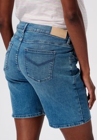 Shorts de mezclilla en azul claro, con un parche trasero y dos bolsillos traseros con un detalle cosido. Rematados a la altura de la rodilla con una textura suave.